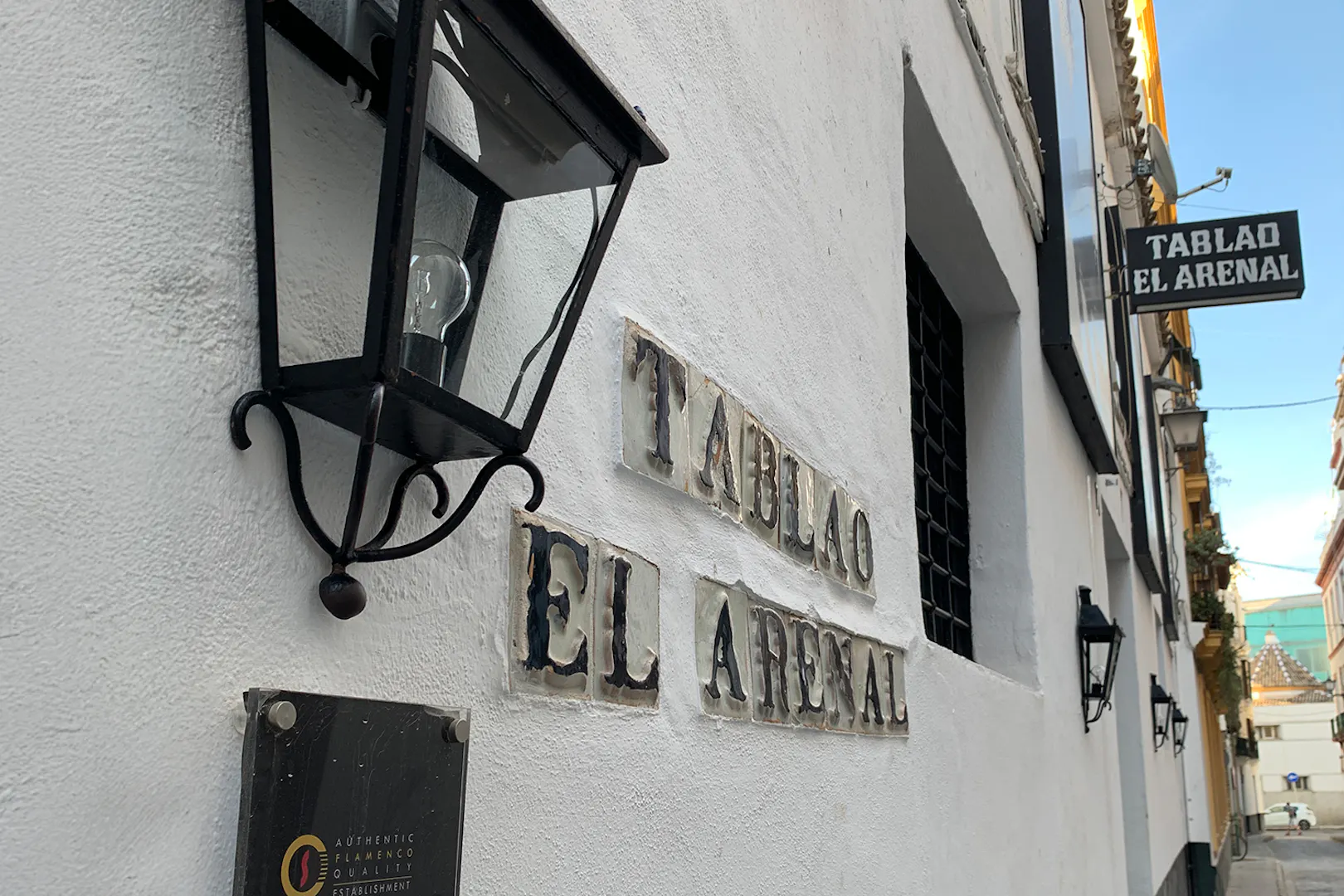 Tablao El Arenal entrance sign on a white building wall in Seville.