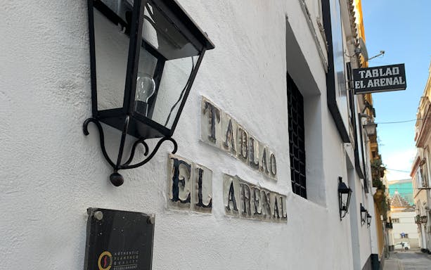 Tablao El Arenal entrance sign on a white building wall in Seville.