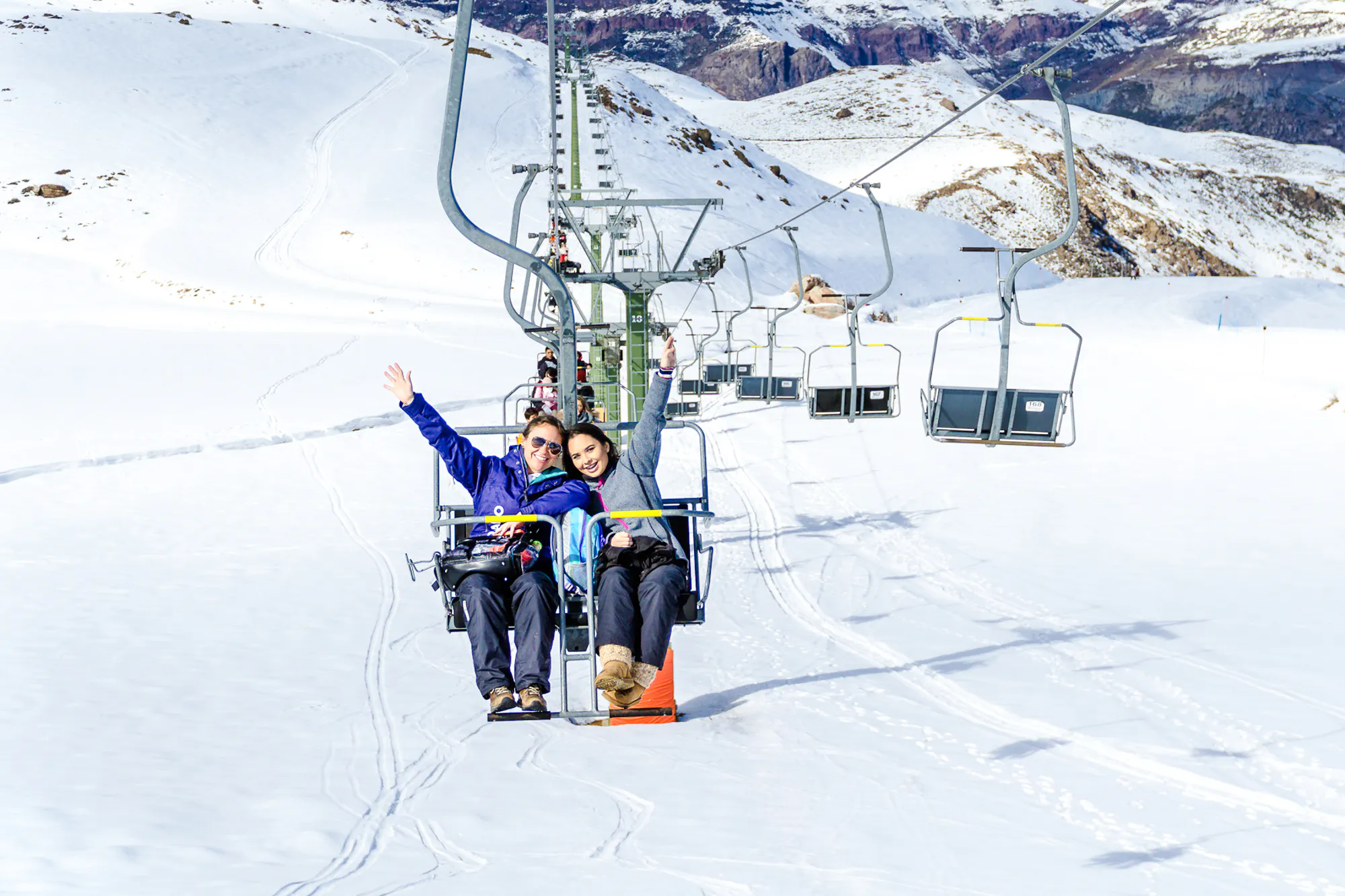 Skiers on a chairlift at Farellones Ski Resort, Santiago, with snowy mountains in the background.