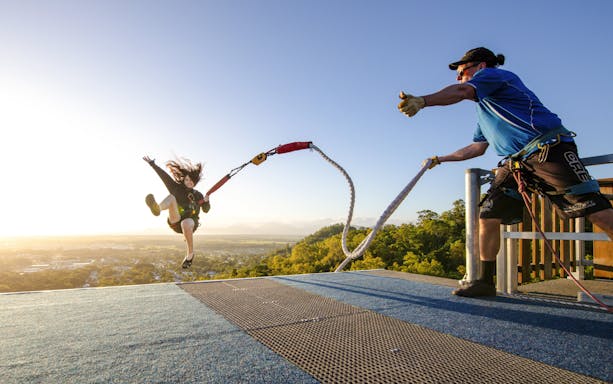 Person jumping off platform during Walk The Plank by AJ Hackett with scenic view in background.