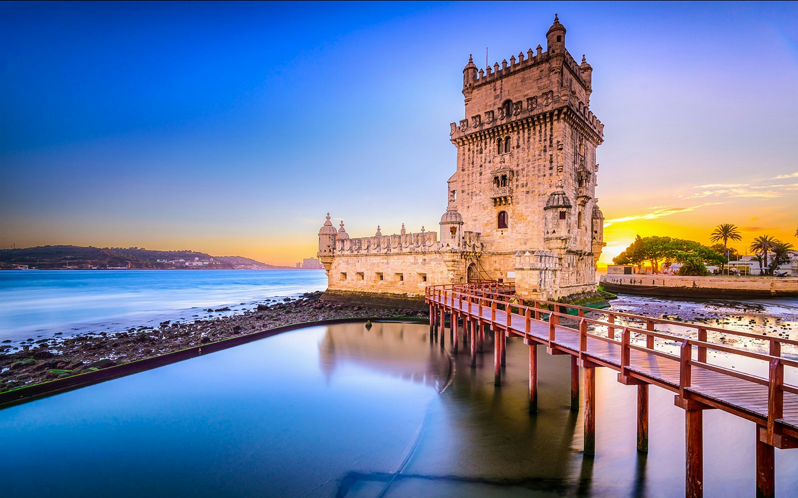Belem Tower in Lisbon at sunset with a wooden walkway over the water.
