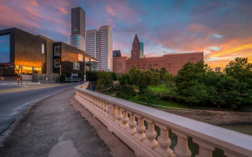 Houston skyline at sunset with modern buildings and a bridge, part of the Haunted Houston exploration game.