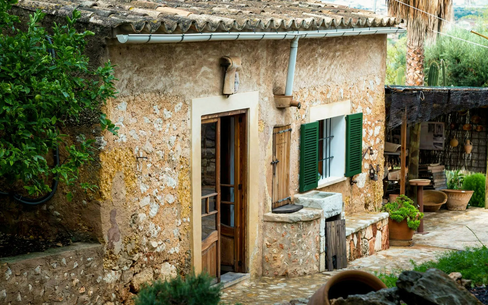 Stone building at a Majorca winery estate with open wooden door and green shutters.