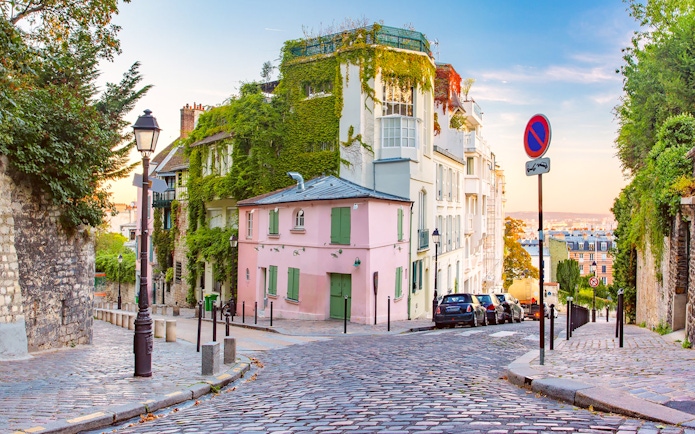 Cobblestone street in Montmartre, Paris, with ivy-covered buildings and a view of the city.