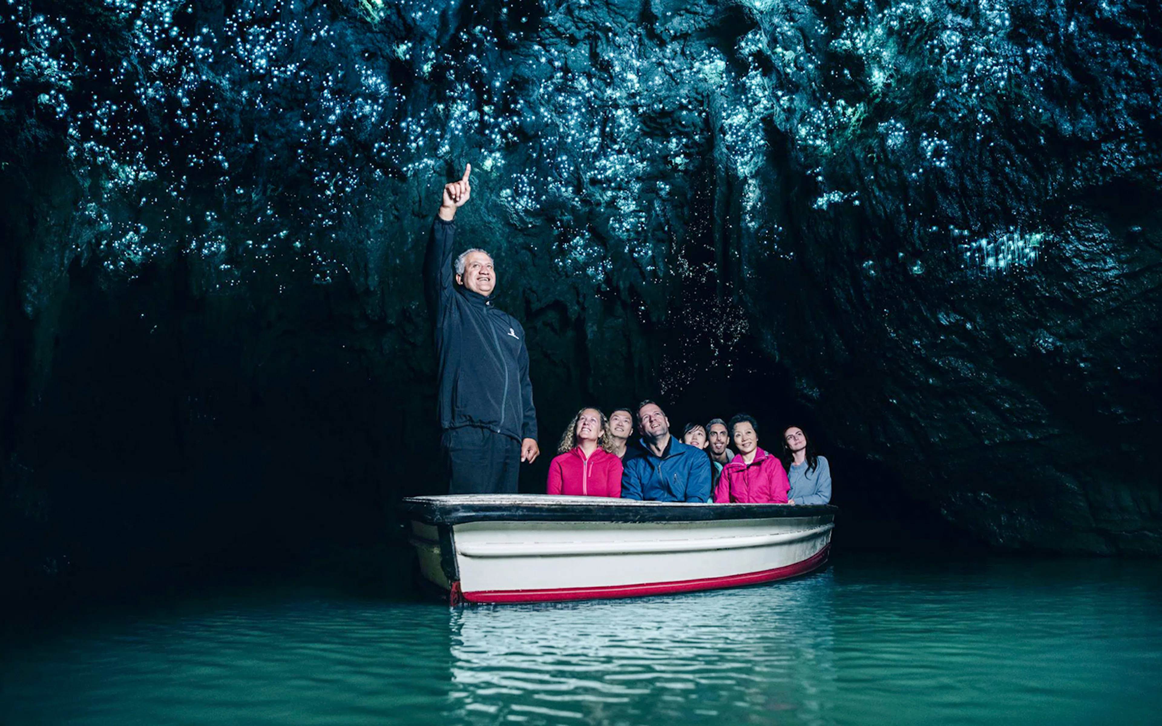 Boat tour in Waitomo Caves with guide pointing at glowworms on cave ceiling.