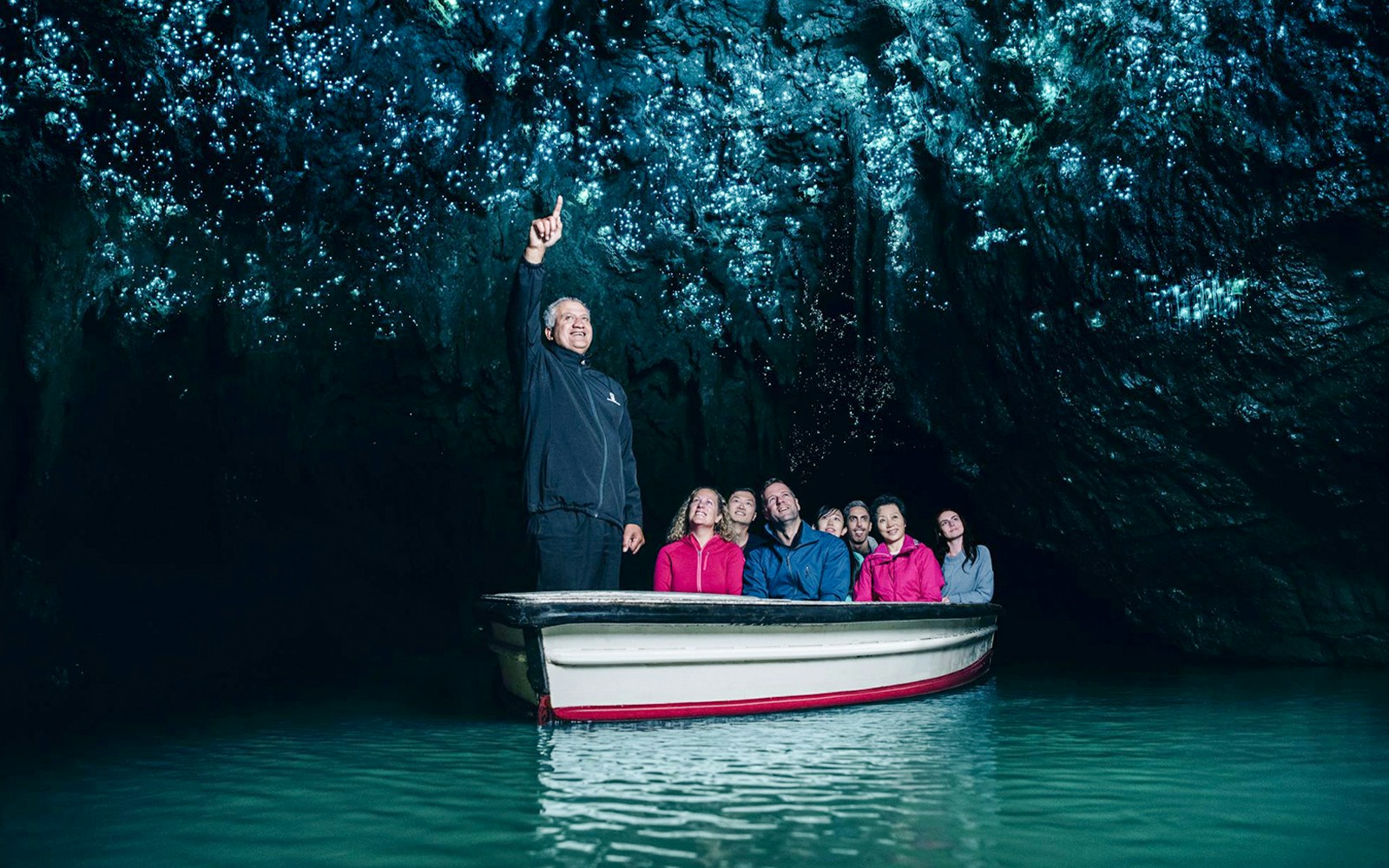Boat tour in Waitomo Caves with guide pointing at glowworms on cave ceiling.