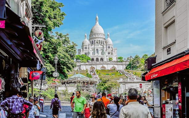 Montmartre street view with Sacré-Cœur Basilica in Paris, bustling with tourists.