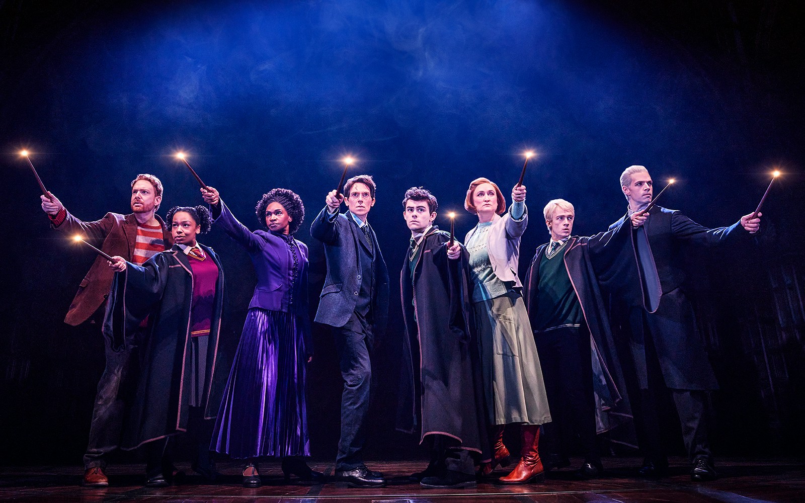 Cast of "Harry Potter and the Cursed Child" holding wands on stage.