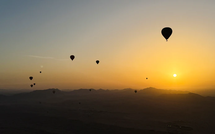 Hot air balloons silhouetted against sunrise over Marrakech landscape.