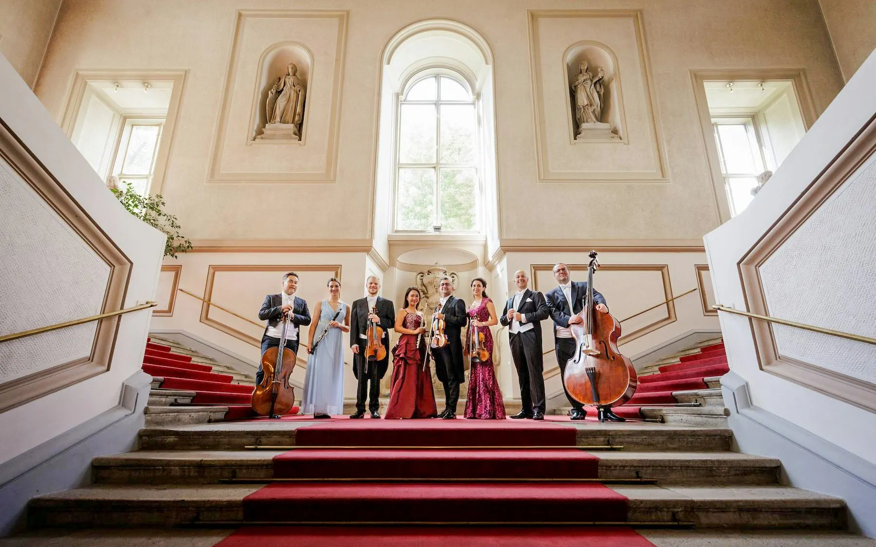 Musicians with instruments on red-carpeted stairs at Palais Auersperg, Vienna.
