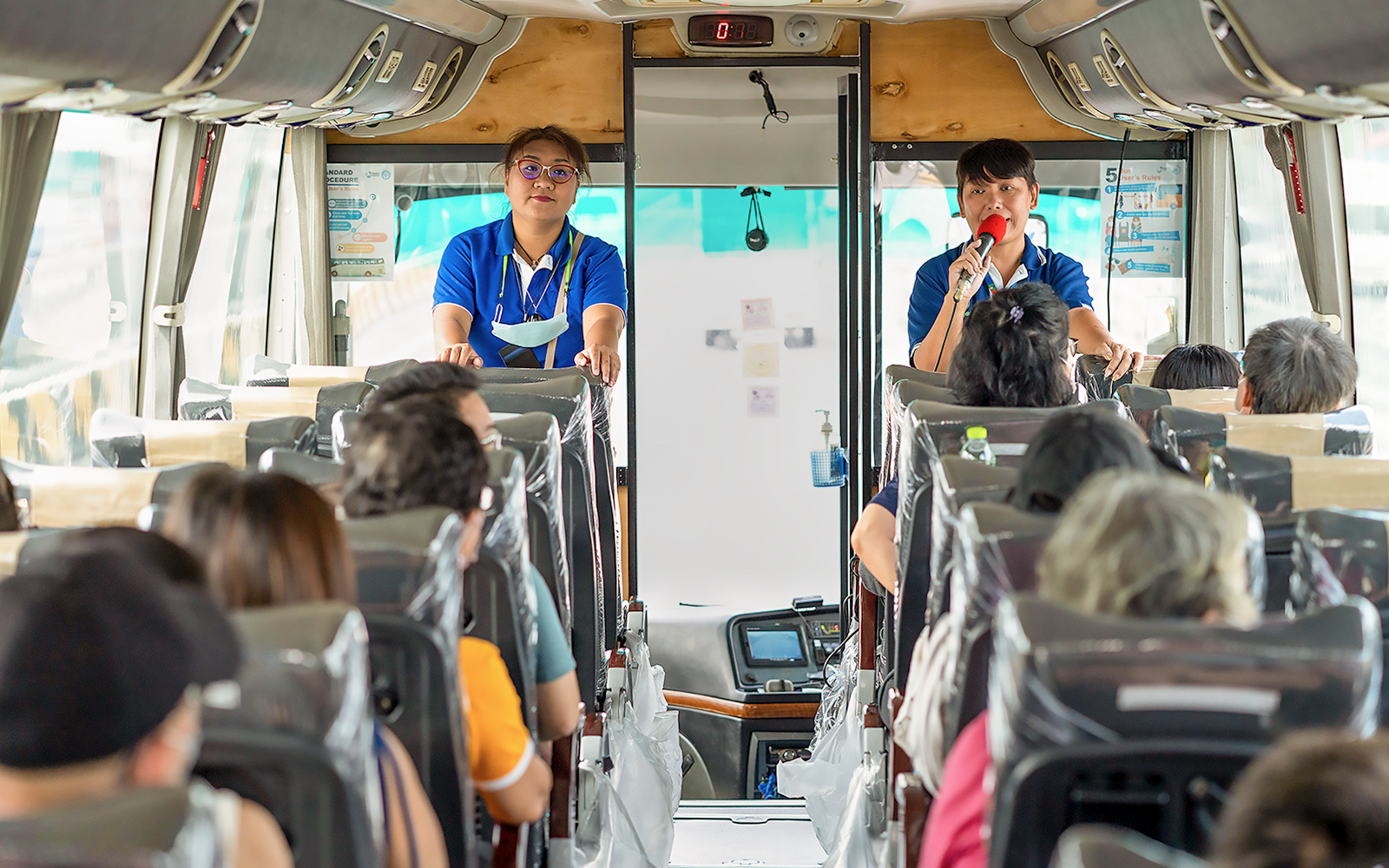 Tour guide speaking to passengers on a bus for Damnoen Saduak Floating Market tour.