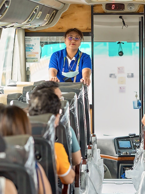 Tour guide speaking to passengers on a bus for Damnoen Saduak Floating Market tour.