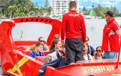 Group preparing for jet boat ride on a river, guided by instructors in red shirts.