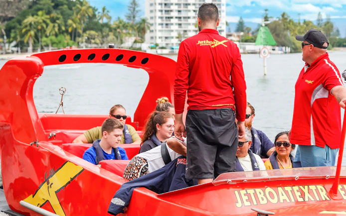 Group preparing for jet boat ride on a river, guided by instructors in red shirts.
