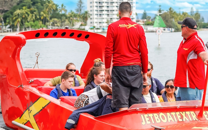 Group preparing for jet boat ride on a river, guided by instructors in red shirts.