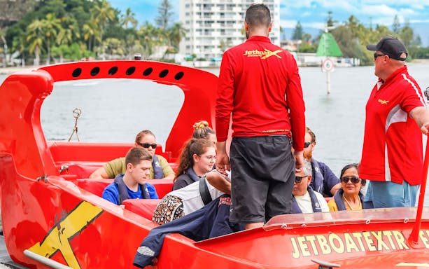 Group preparing for jet boat ride on a river, guided by instructors in red shirts.