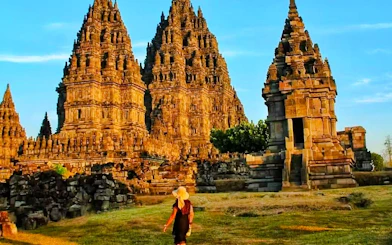 Prambanan Temple complex with visitor walking on grassy path, Yogyakarta, Indonesia.