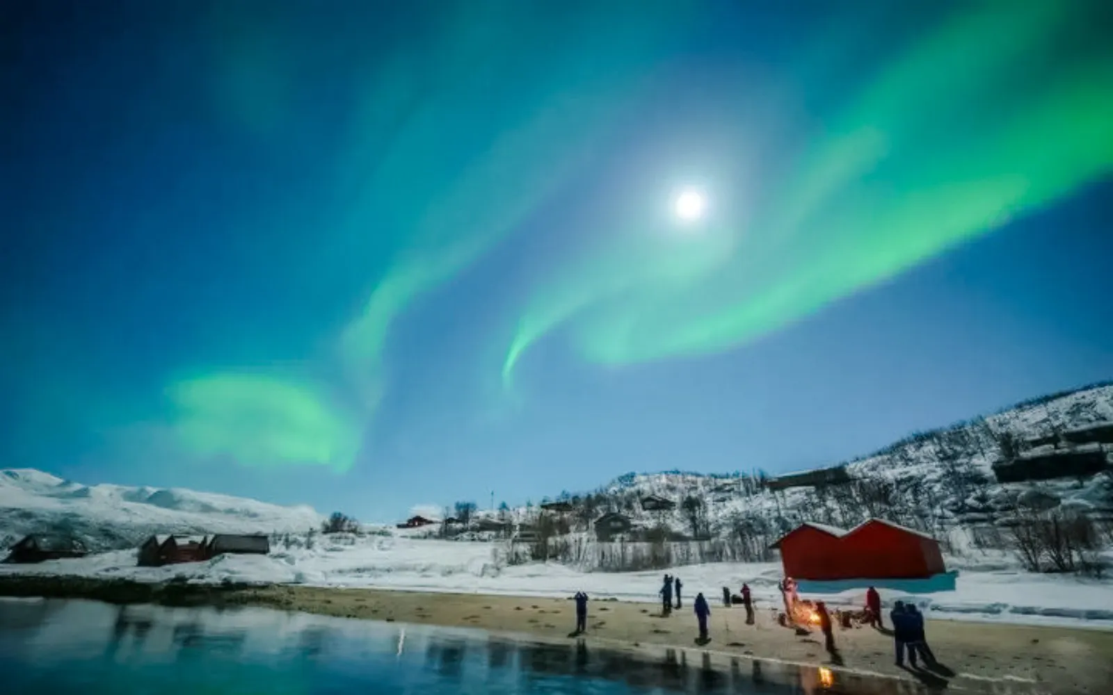 Guests viewing northern lights on Tromso tour with snowy landscape and cabins.