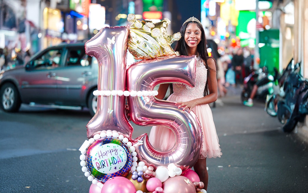 Young woman celebrating 15th birthday with balloons at Times Square, New York City.