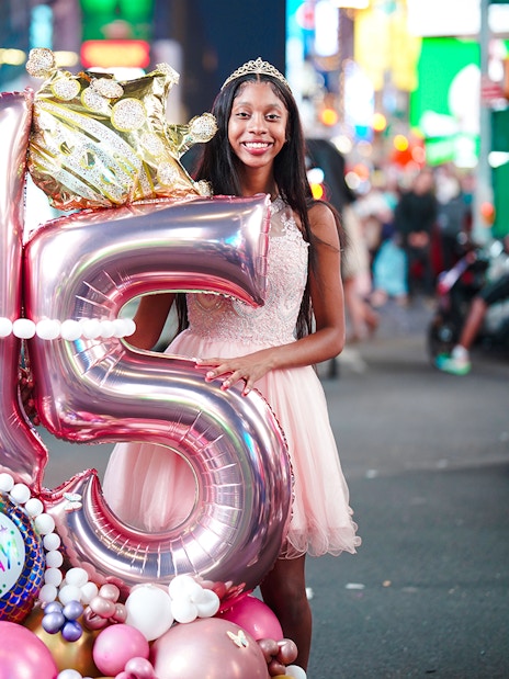 Young woman celebrating 15th birthday with balloons at Times Square, New York City.
