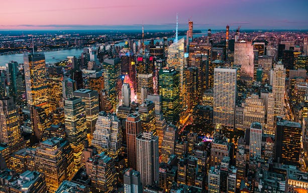 Aerial view of New York City skyline at dusk with illuminated skyscrapers.