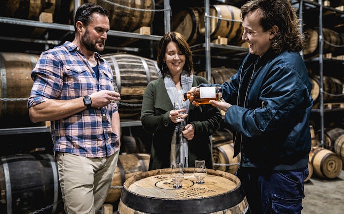 Visitors enjoying a whiskey tasting at a distillery in Tasmania, surrounded by barrels.