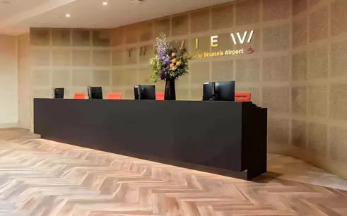 Reception desk at The View Brussels Airport Lounge with computers and floral arrangement.