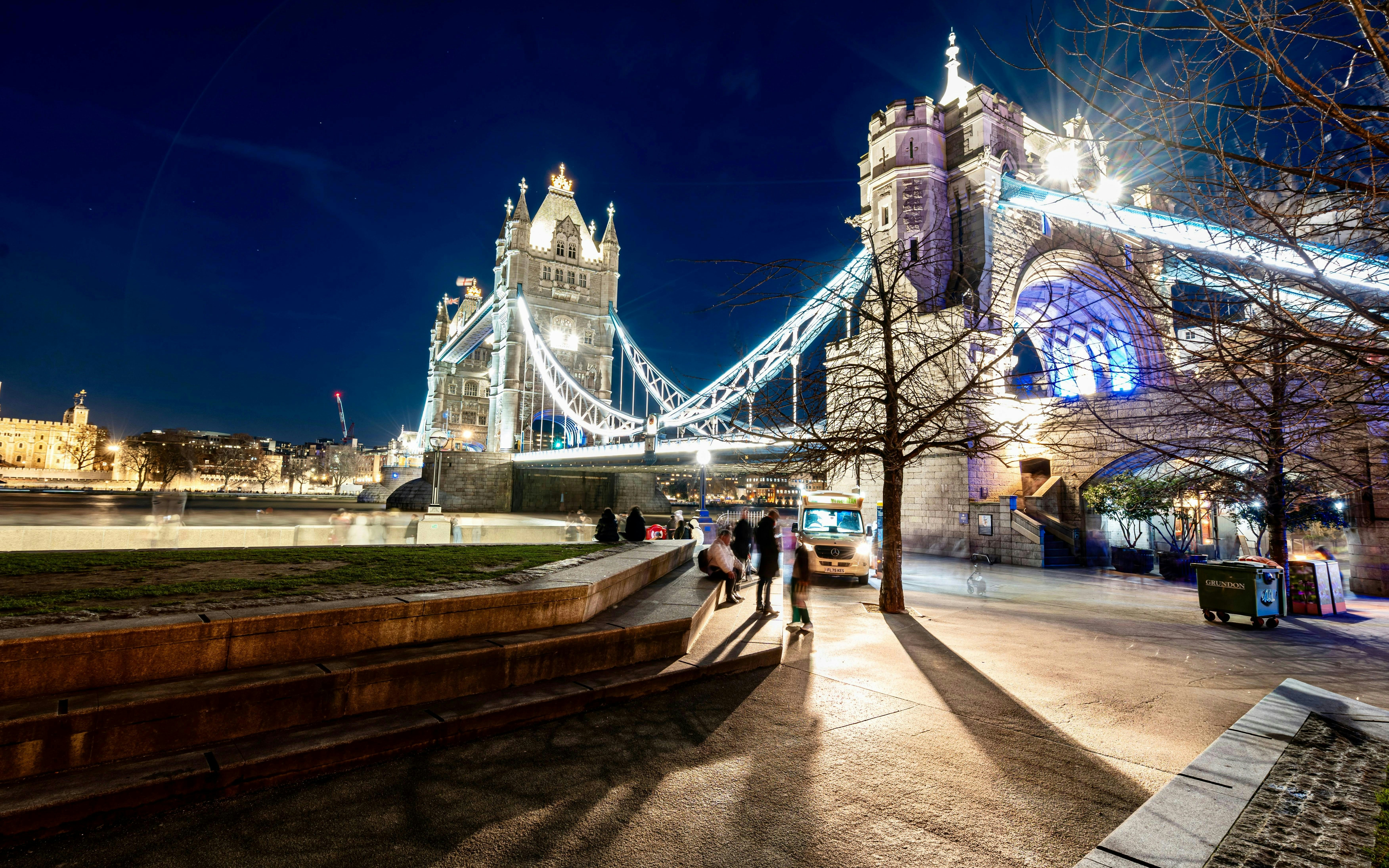 Tower Bridge illuminated at night in London with people walking nearby.