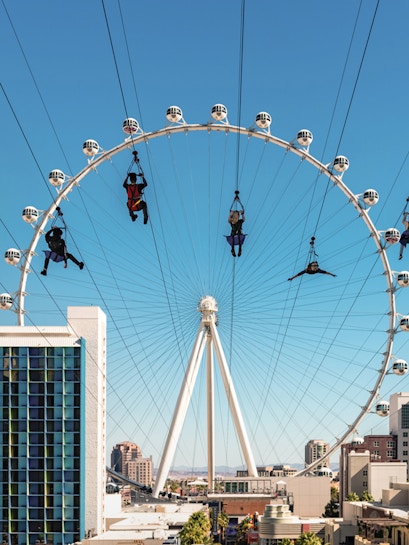People ziplining in front of the High Roller observation wheel in Las Vegas on the Fly LINQ Zipline.