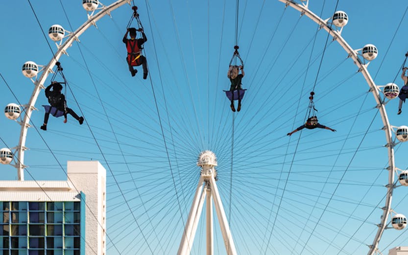 People ziplining in front of the High Roller observation wheel in Las Vegas on the Fly LINQ Zipline.