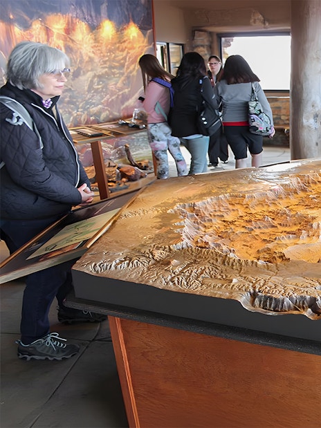Grand Canyon South Rim visitors examining a detailed topographic model in an indoor exhibit.
