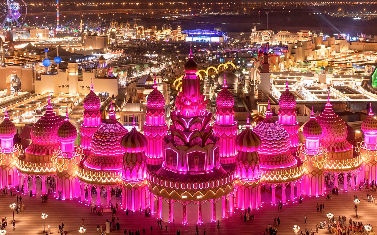 Global Village Dubai illuminated pavilions at night with visitors exploring.