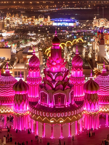 Global Village Dubai illuminated pavilions at night with visitors exploring.