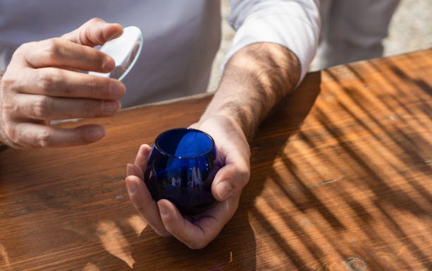 Hands holding a blue glass for olive oil tasting in Santorini.
