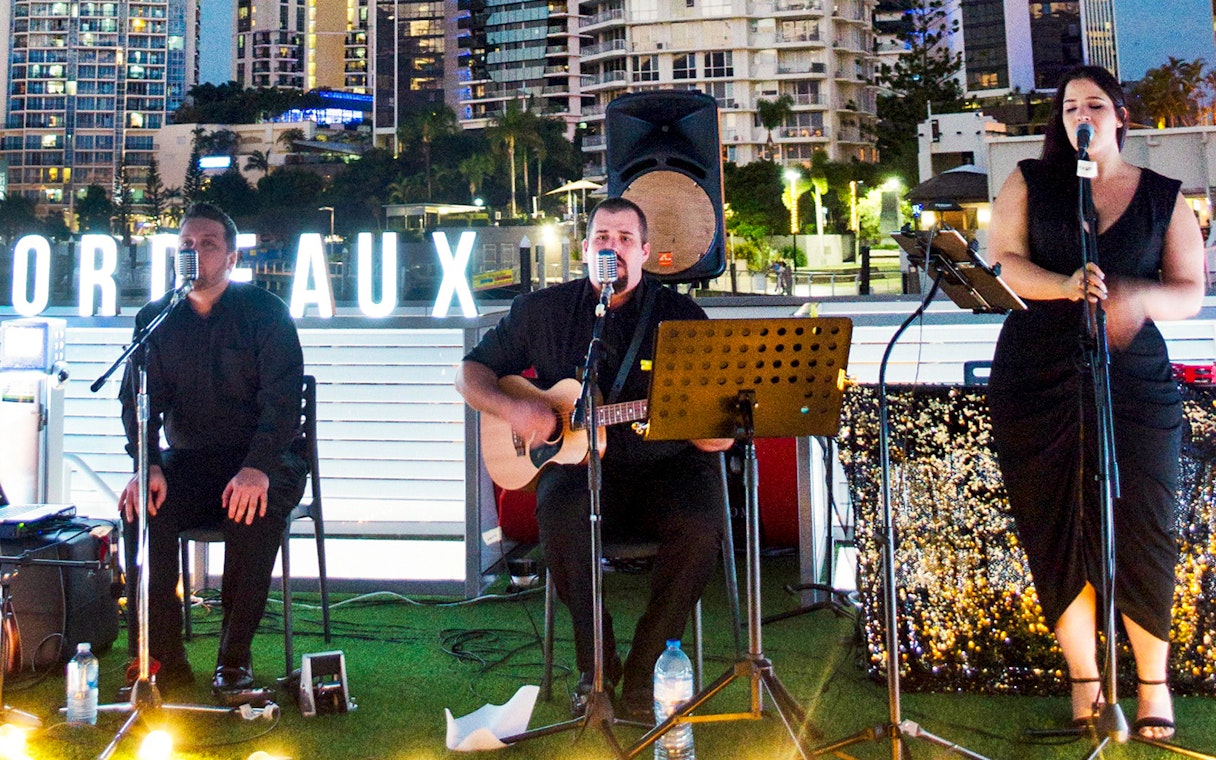 Musicians performing on a buffet dinner cruise in Bordeaux with city skyline backdrop.