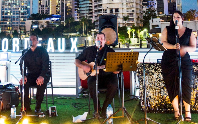 Musicians performing on a buffet dinner cruise in Bordeaux with city skyline backdrop.