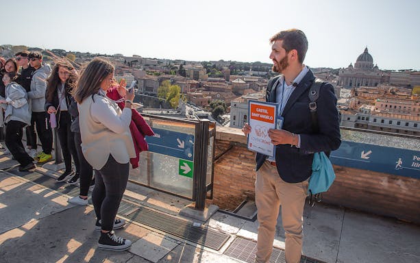 Tour guide holding Castel Sant’Angelo sign with tourists overlooking Rome.