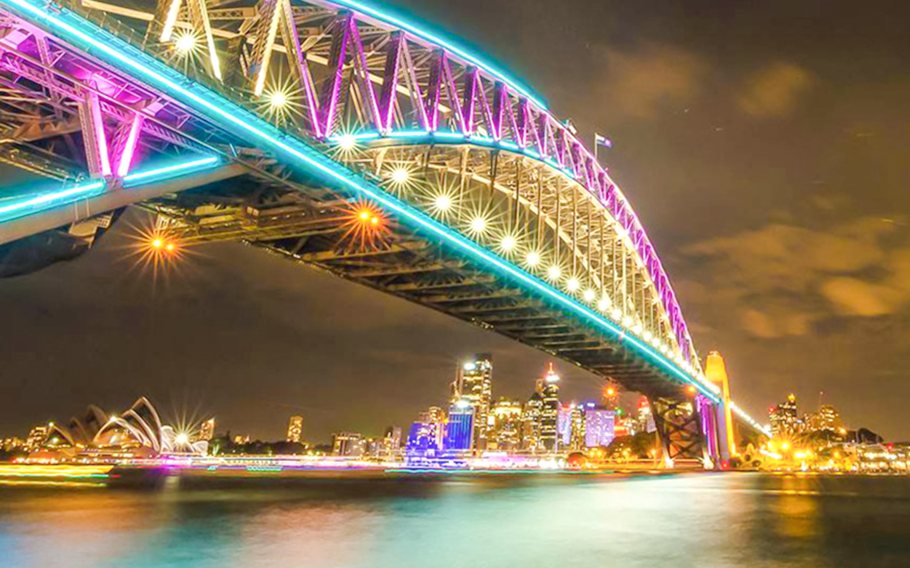 Sydney Harbour Bridge illuminated during Vivid Sydney festival, viewed from a luxury cruise.
