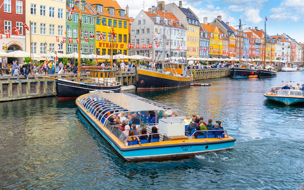 Canal tour boat in Nyhavn, Copenhagen, passing colorful buildings and docked ships.