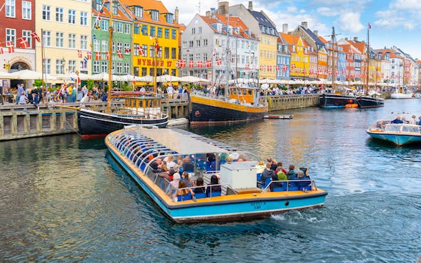 Canal tour boat in Nyhavn, Copenhagen, passing colorful buildings and docked ships.