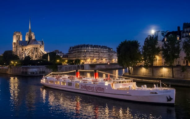 Dinner cruise boat on the Seine River with Notre-Dame Cathedral in the background, Paris.