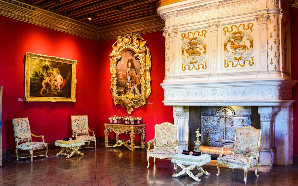 Interior of Château de Chenonceau with ornate fireplace, red walls, and classic paintings, Loire Valley.