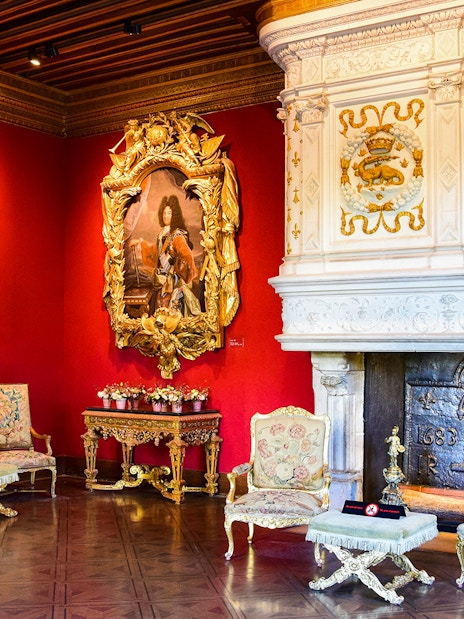 Interior of Château de Chenonceau with ornate fireplace, red walls, and classic paintings, Loire Valley.