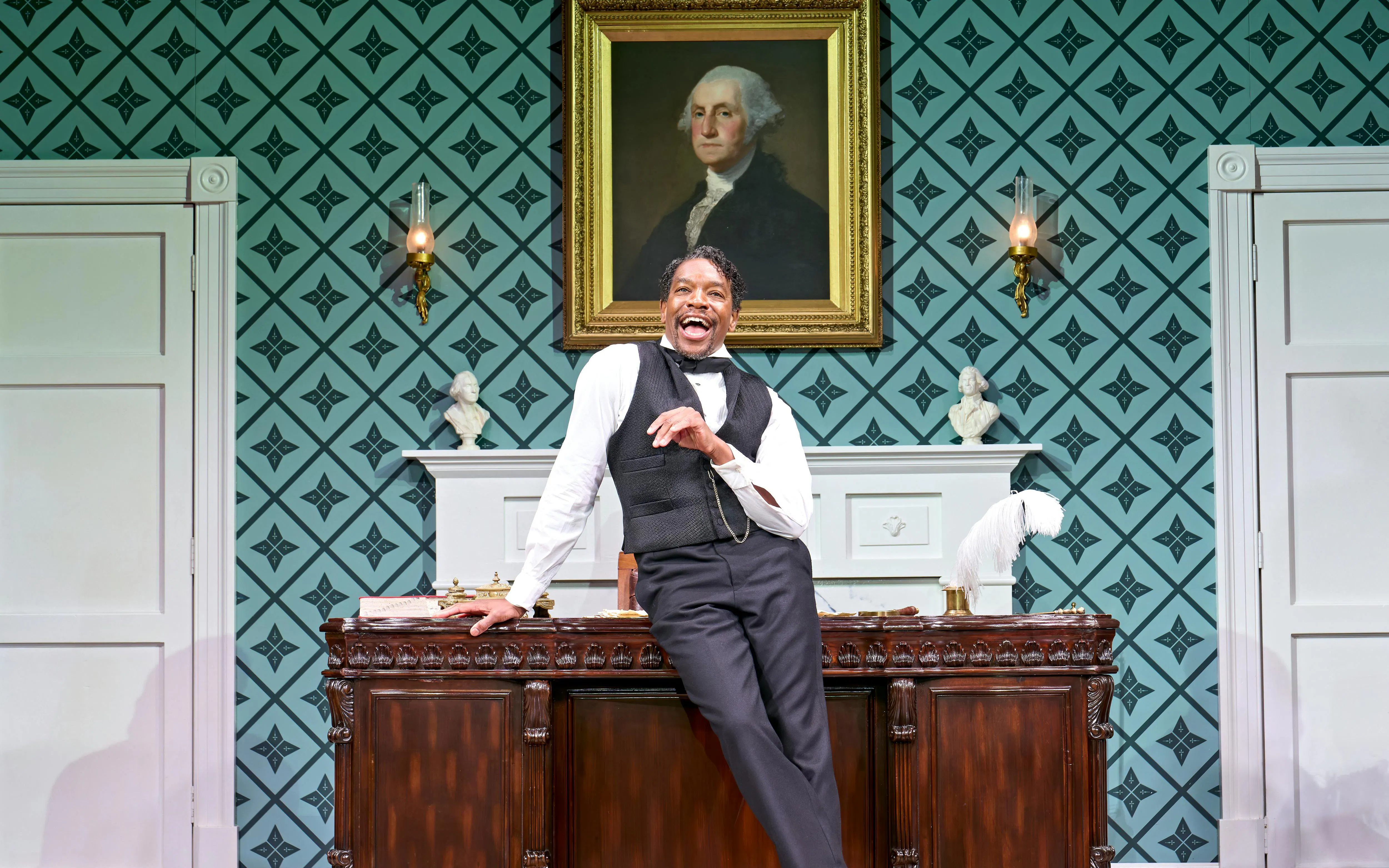 Actor performing in "Oh Mary" at West End theater, standing by a vintage desk with a portrait behind.