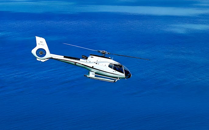 Helicopter flying over blue water in Dubai.