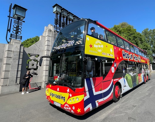 Red double-decker bus on a Hop on Hop off tour in Oslo, passing by historic buildings and city streets.