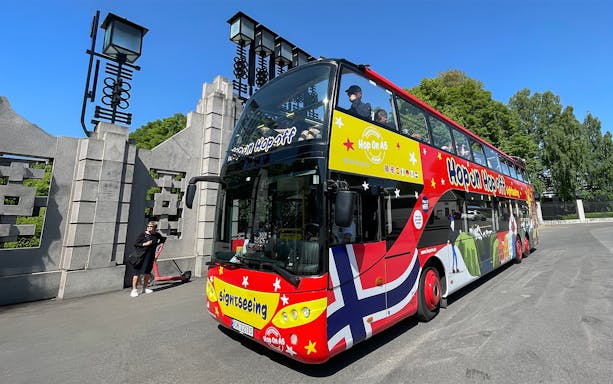 Colorful double-decker bus for Hop on Hop off tour in Oslo, parked near a stone gate.