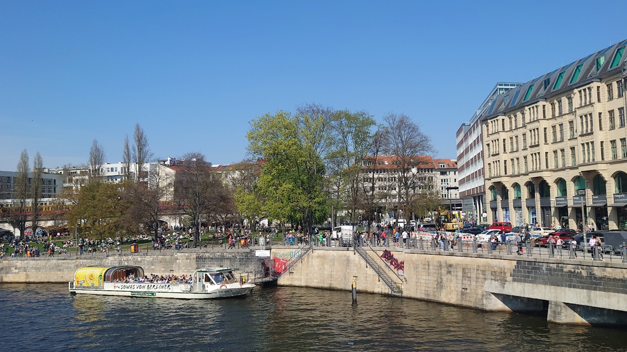 Sightseeing boat on the River Spree in Berlin with people enjoying the riverside.