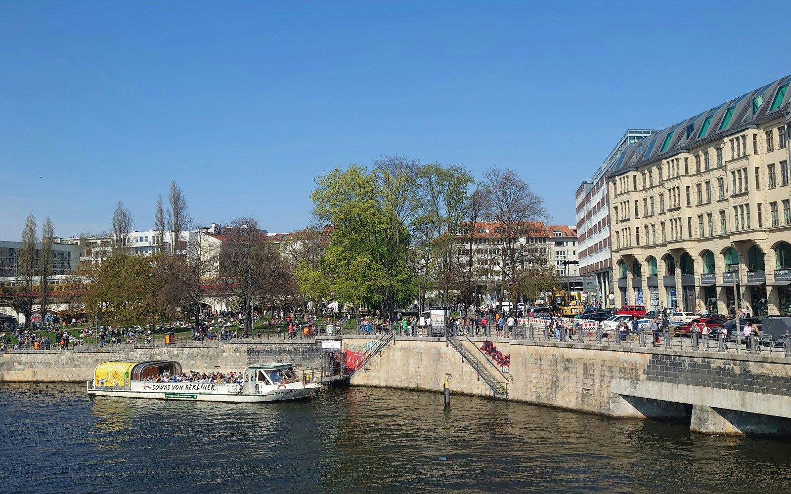 Sightseeing boat on the River Spree in Berlin with people enjoying the riverside.