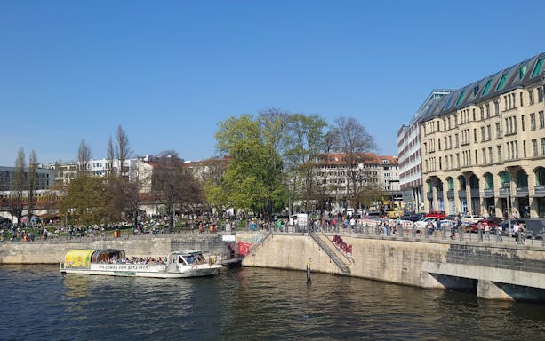 Sightseeing boat on the River Spree in Berlin with people enjoying the riverside.